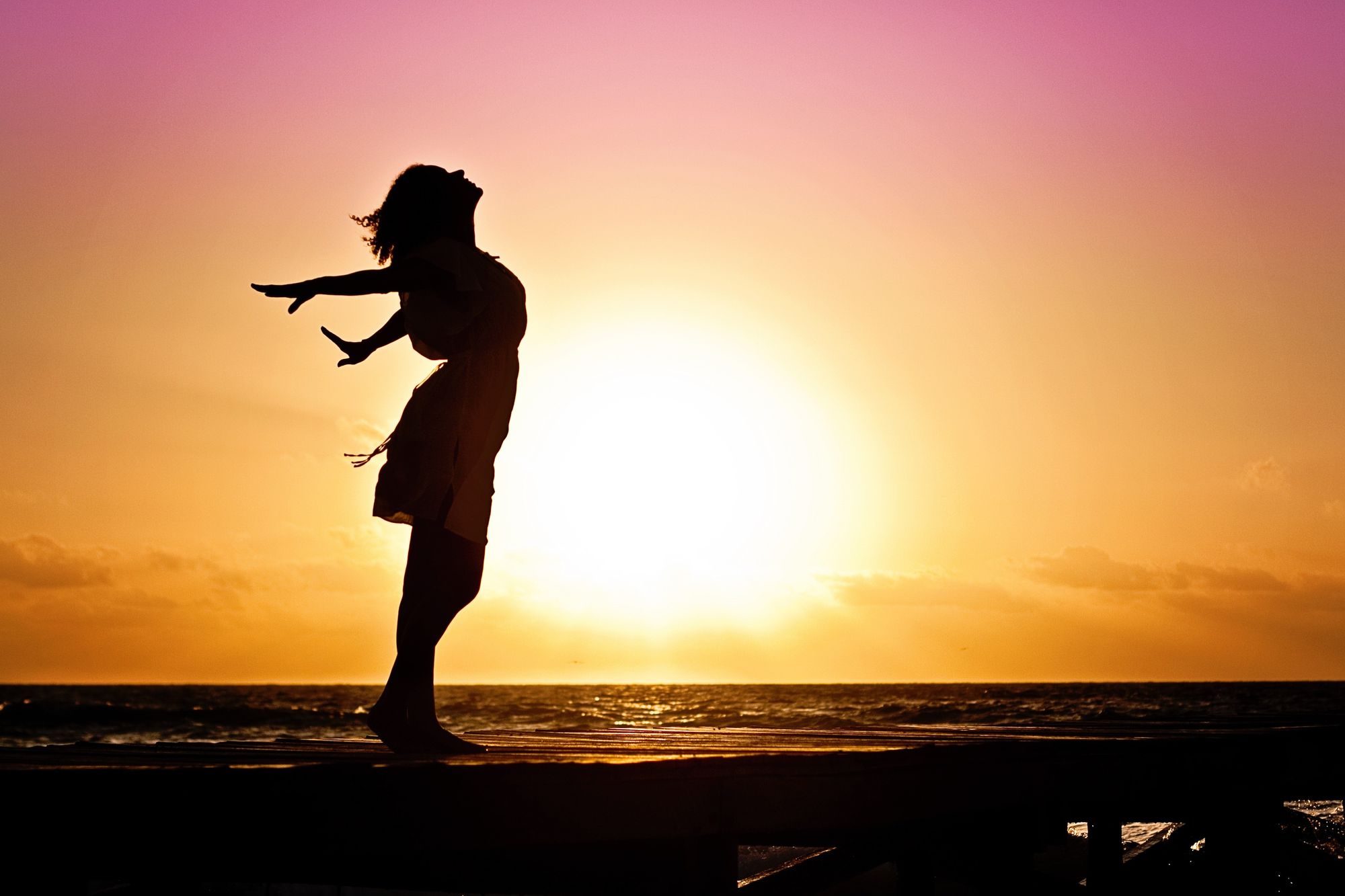 Mujer en un muelle al lado del mar durante el atardecer