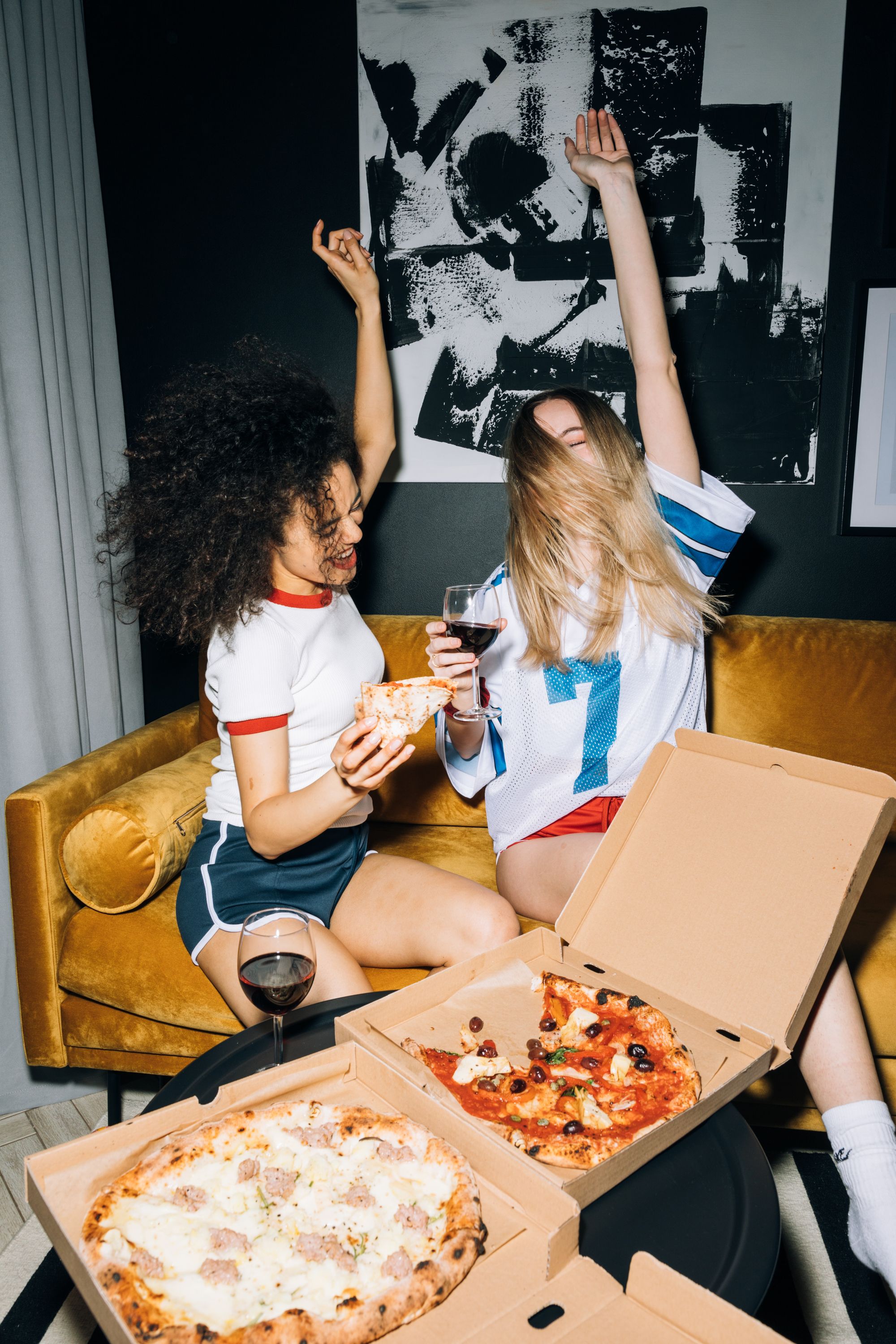 2 mujeres jovenes comiendo pizza y bebiendo vino en una noche cannábica